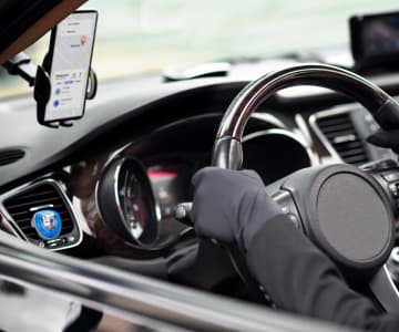 Driver's hand on a steering wheel with a mounted smartphone displaying a taxi service app